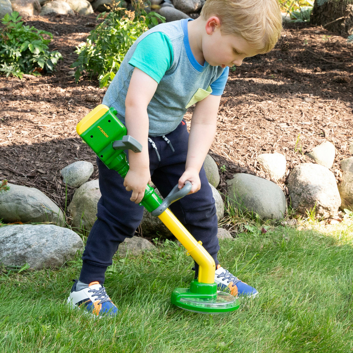 Child playing with a John Deere Weed Trimmer Toy in a garden setting