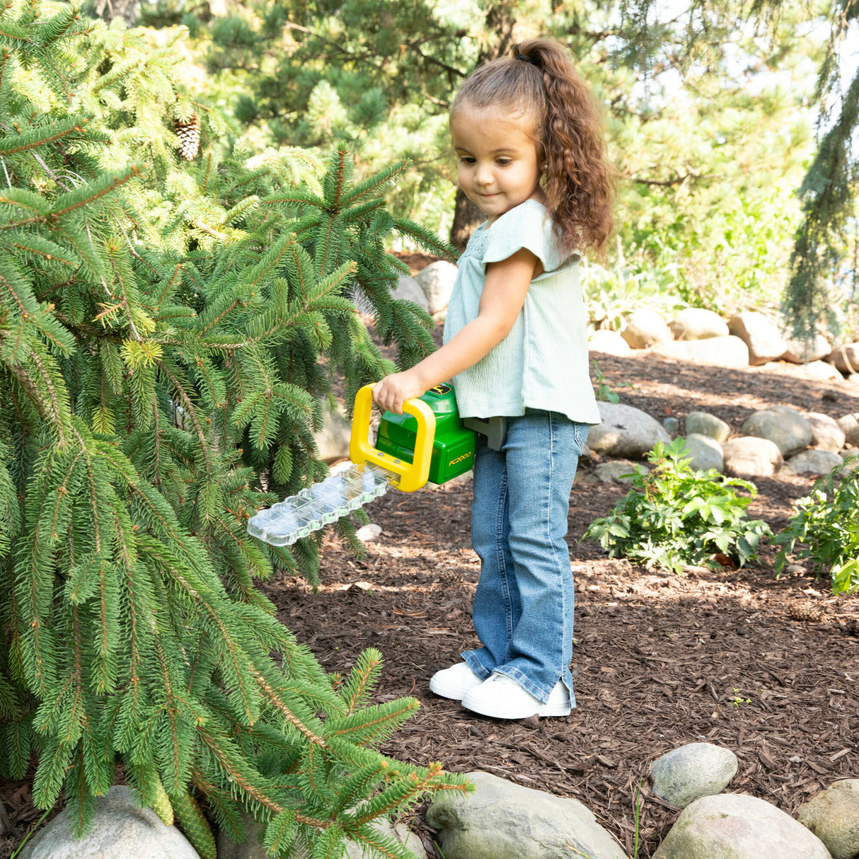 Child playing with a John Deere Hedge Trimmer Toy in a garden setting
