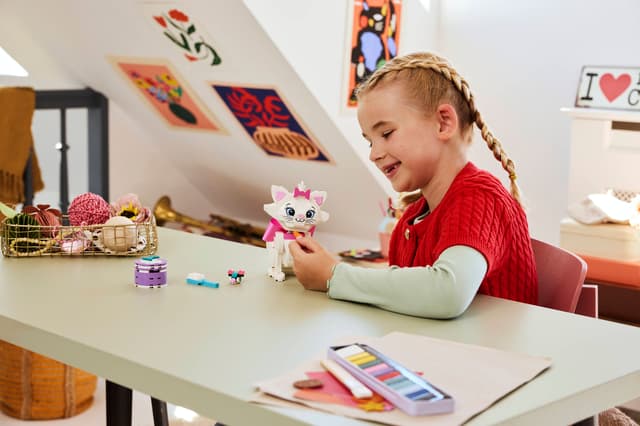 Child playing with a LEGO Disney Classic: The Aristocats Adorable Marie at a desk in a room with colorful decorations