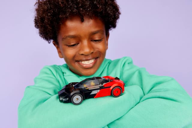 Child holding a LEGO City Great Vehicles: EV Supercar against a light purple background