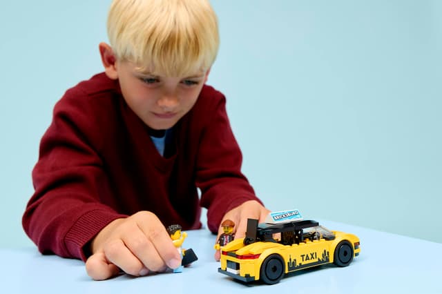 Child playing with a LEGO City Great Vehicles: Yellow Taxi made of building blocks on a light blue background