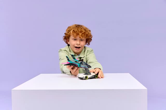 Child holding a toy airplane on a white table with a purple background