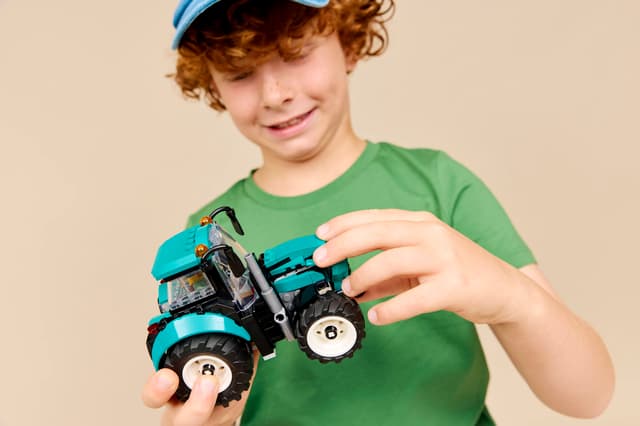 Child holding a LEGO City Great Vehicles: Tractor against a beige background