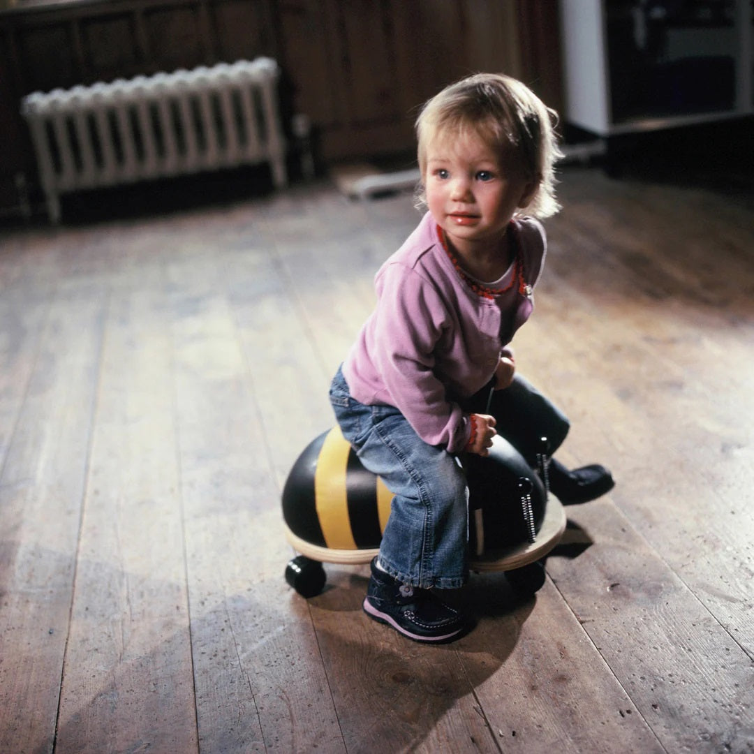 Child riding a Wheely Bug - Bee on a wooden floor