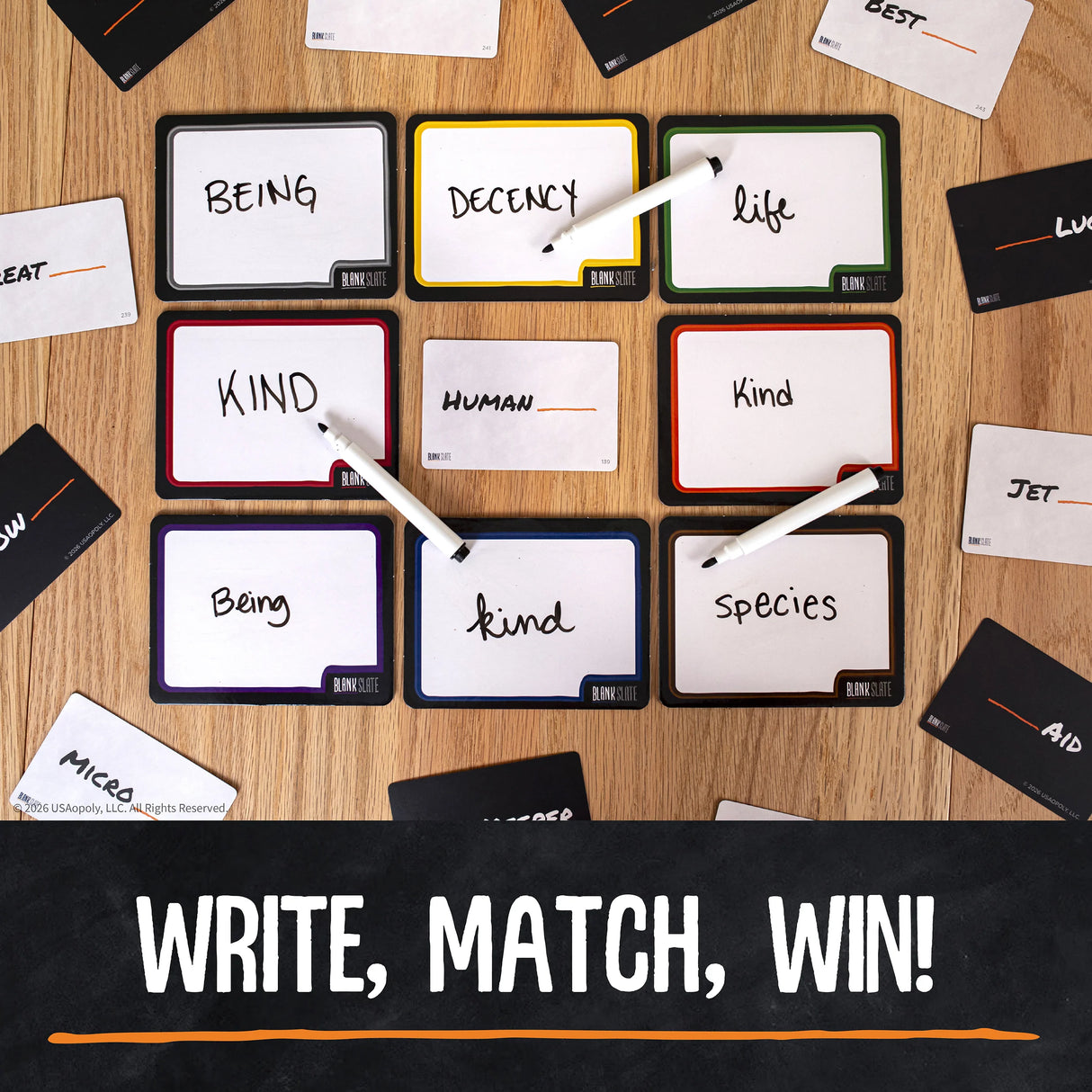 A flat-lay view of a word-matching Blank Slate™ Game board on a wooden surface, with black cards, white writing markers, and several white cards partially visible around the board. A black banner at the bottom reads “WRITE, MATCH, WIN!” in white text.