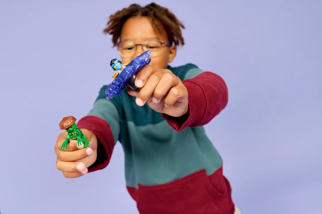 Child holding LEGO Ninjago: Nya vs. Mutation Monster Spinner figures against a purple background