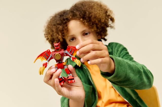 Child holding a LEGO Ninjago: Kai's Dragon Mech Battle Pack figure against a beige background