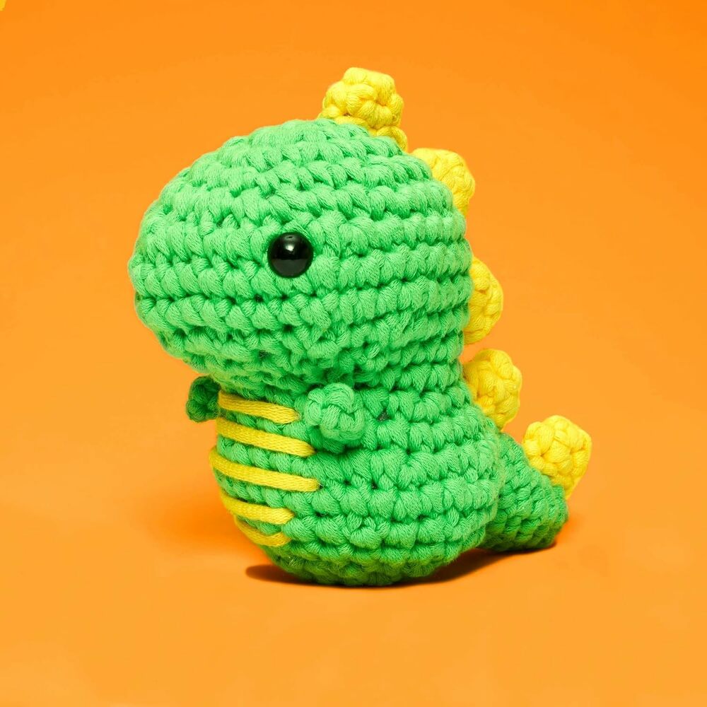 Green and yellow crocheted dinosaur toy on an orange background