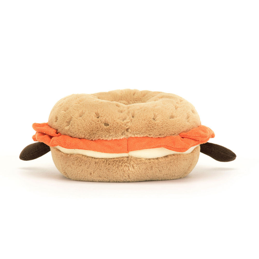 Rear view of a plush Amuseables Bagel toy shaped like a bagel with orange and white filling with brown arms on a white background