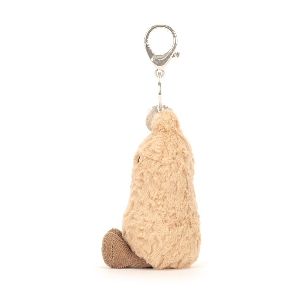 Plush beige peanut-shaped bag charm with a metal clasp and soft textured fabric, designed as a fun accessory for bags or backpacks.