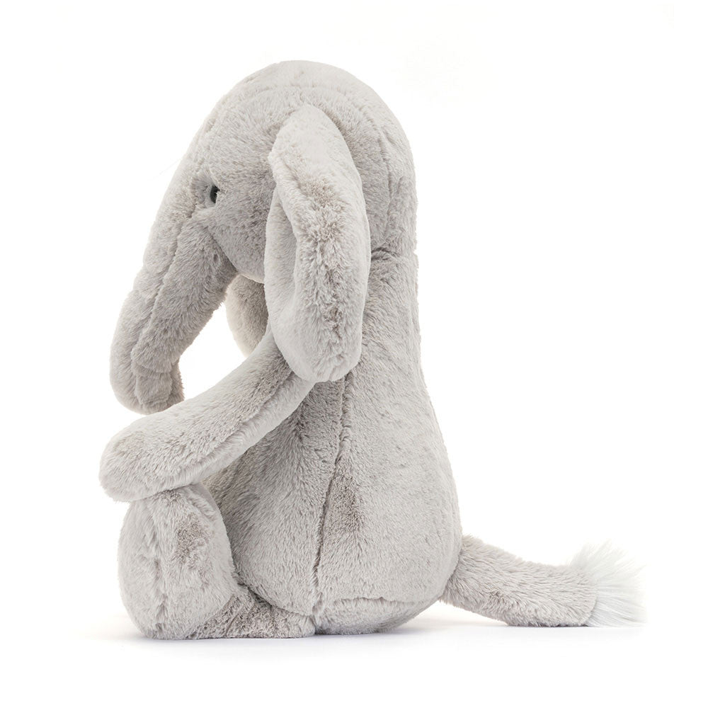Soft and cuddly plush stuffed elephant sitting upright with large floppy ears and a tufted tail, perfect as a kid's gift or nursery decor, called Bashful Luxe Elephant Thuddeus Huge.
