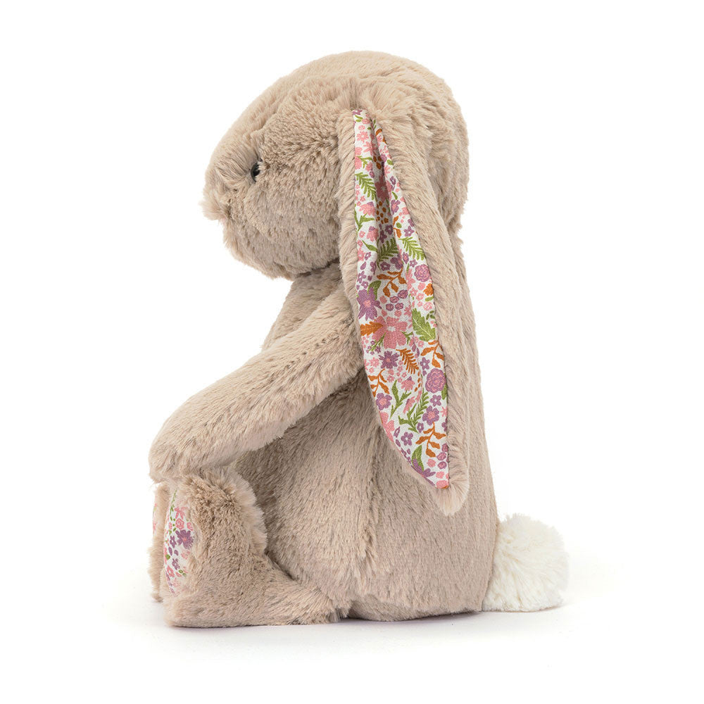 Side view of a plush Blossom Beige Bunny 'Petal' toy with floral ear on a white background