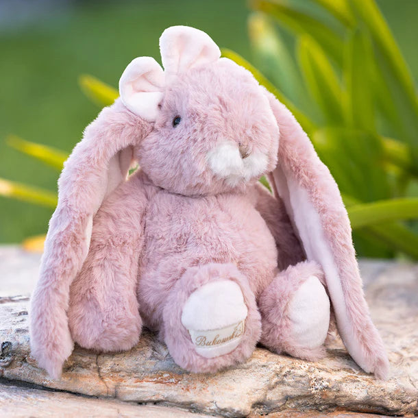 Pink plush Friendly Kanina - Antique Pink bunny sitting on a wooden log with a blurred green background