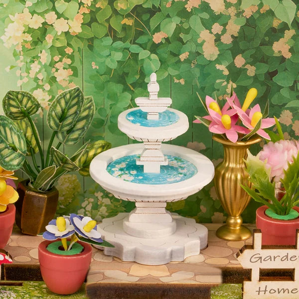 Miniature garden scene with a fountain, plants, and flowers against a green foliage background from the Green Fountain Garden, Super Mini Houses craft kit.