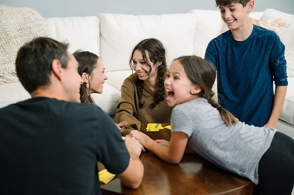 Family of five sitting on a couch with a young girl excitedly reaching out towards a table.