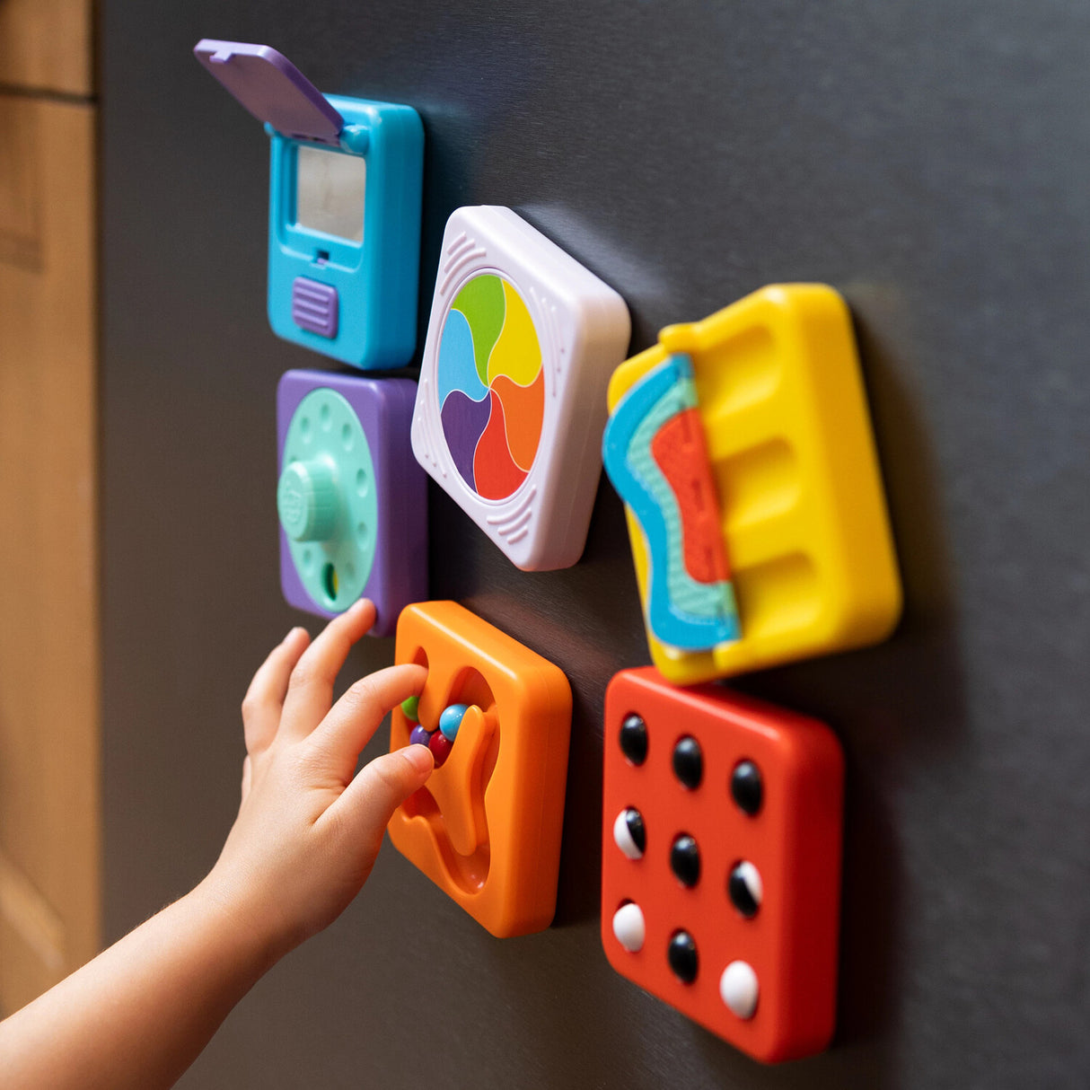 Colorful PlayTab Tiles Set 1 on a refrigerator with a child's hand interacting with one of them.