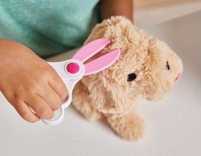 Child's hand holding a toy pair of scissors near a plush dog toy on a light background