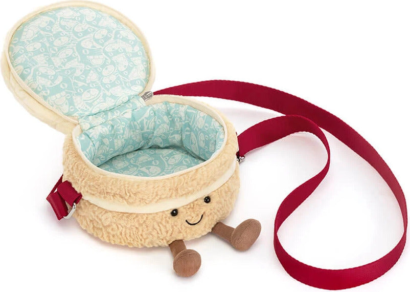 A plush Amuseables Birthday Cake Bag featuring a cream-colored textured exterior, a light blue patterned interior lining, a red strap, and small wooden legs.