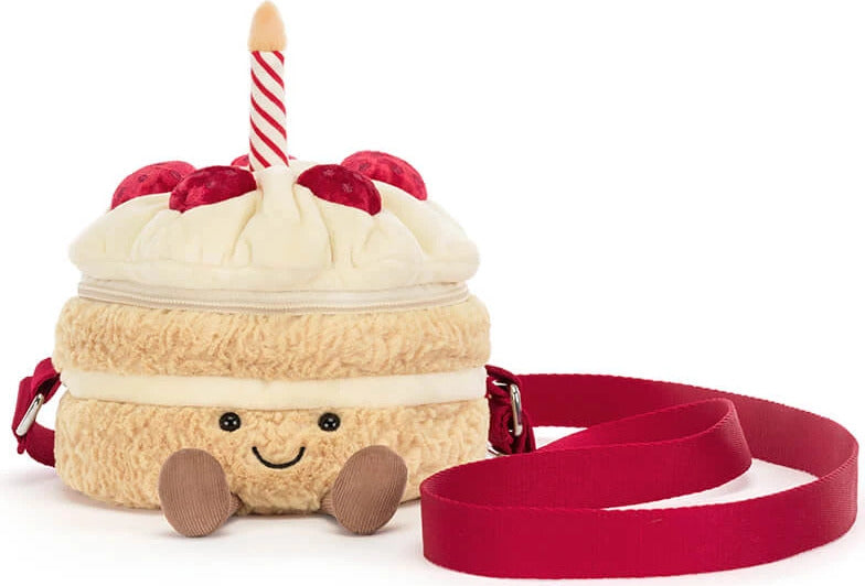 A plush Amuseables Birthday Cake Bag with a smiling face, cream frosting, red cherries, a red-and-white candle, and a red shoulder strap on a white background.