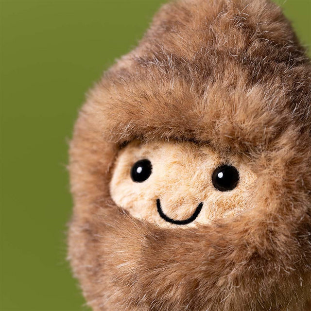 Close-up of a plush Amuseables Peanut Yeti Outfit toy with a brown fuzzy exterior and beige face on a green background