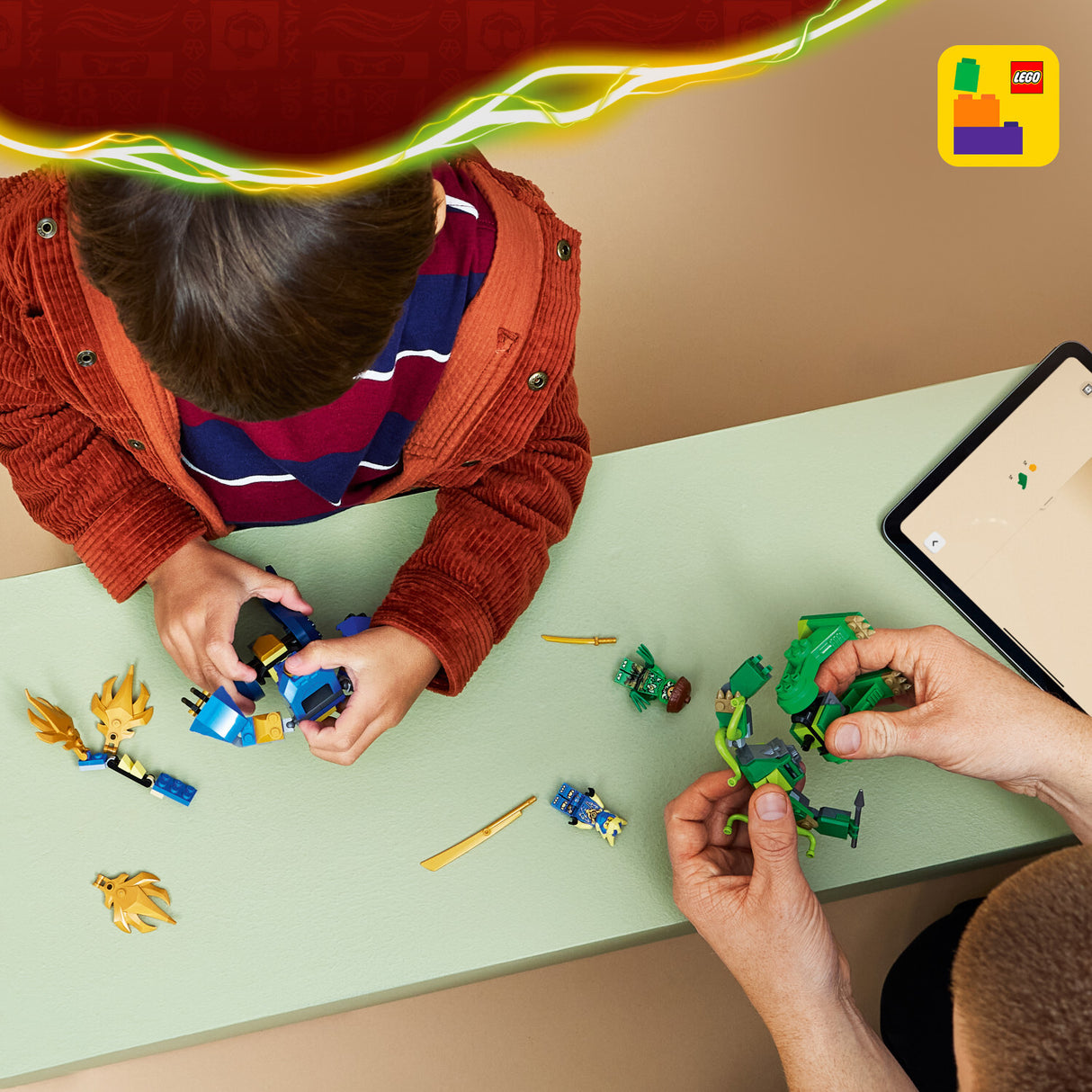 Two people playing with LEGO LEGO Ninjago: Jay's Dragon Mech Fight set at a table, with a tablet displaying a LEGO app in the background.