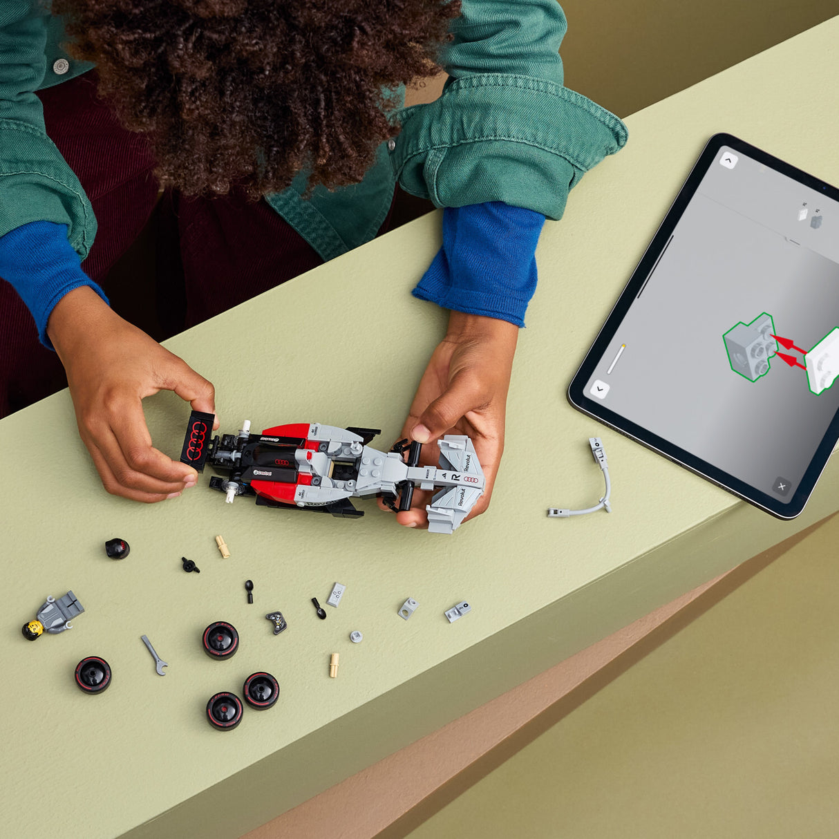 Children playing with aLEGO Speed Champions: Audi Revolut F1® Team R26 Race Car set on a table with a tablet displaying a design.