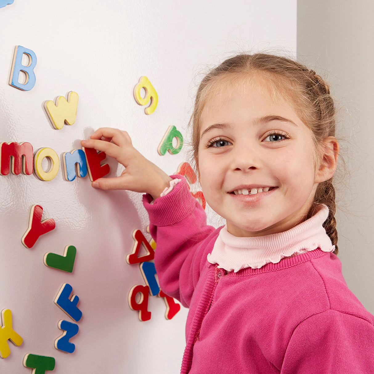 Child playing with colorful magnetic letters on a white board