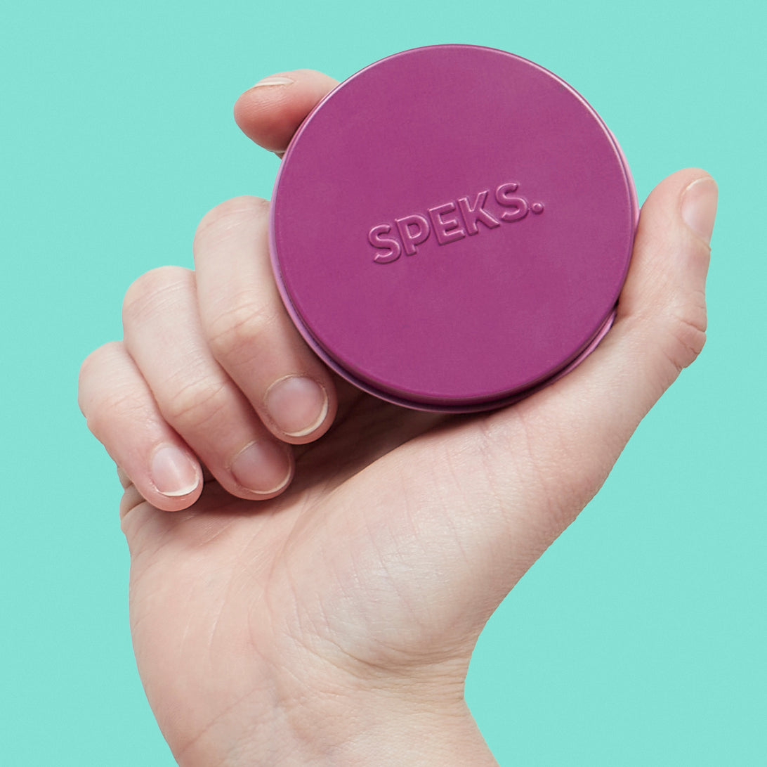 Hand holding a purple Mini Matte Crags Iris tin against a light blue background