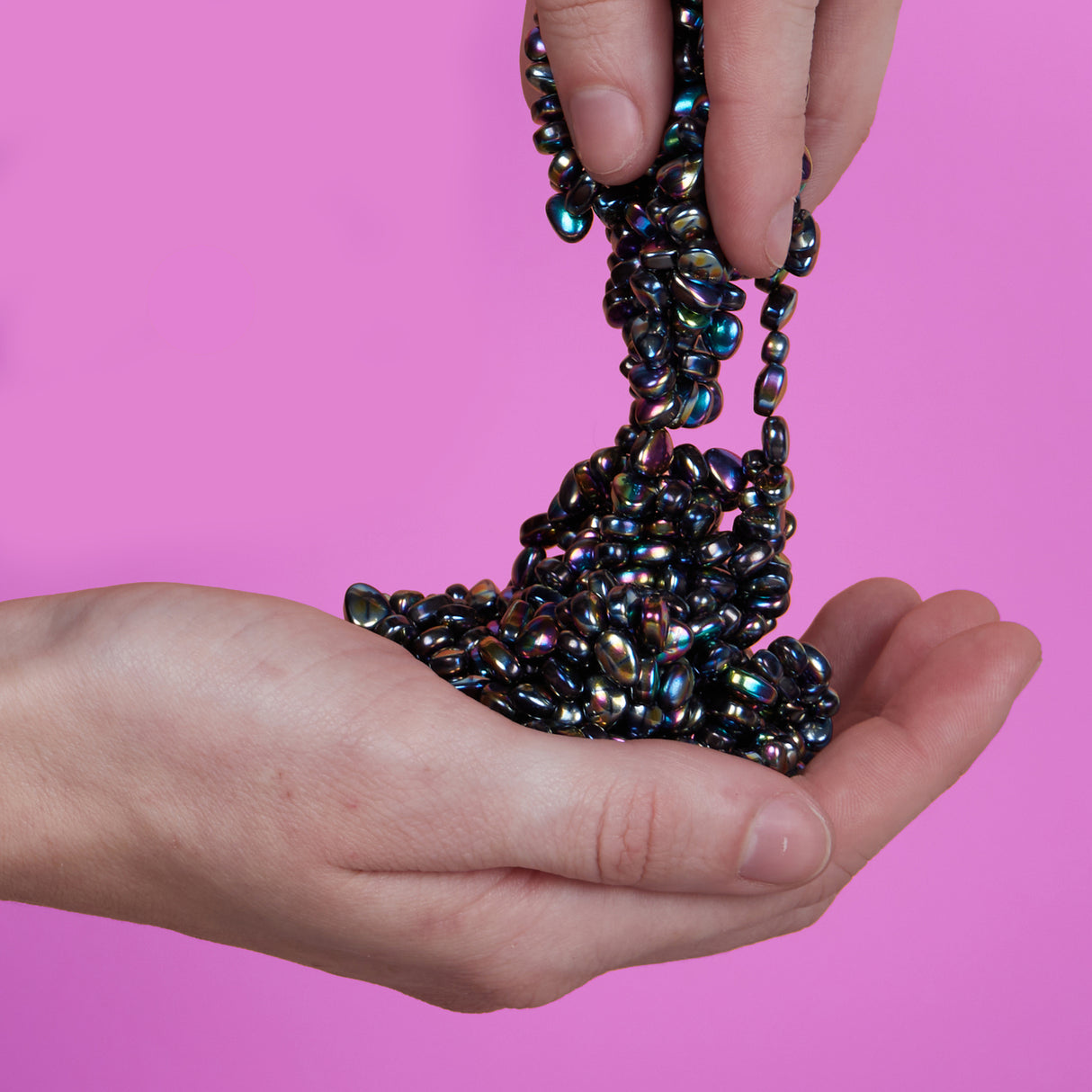 Hand holding a cluster of Medium Crags Oil Slick against a pink background