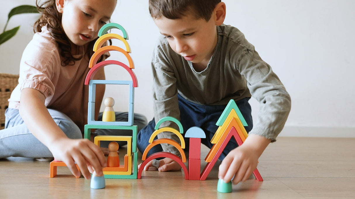 Two children playing with Rainbow Wooden Blocks on a wooden floor.
