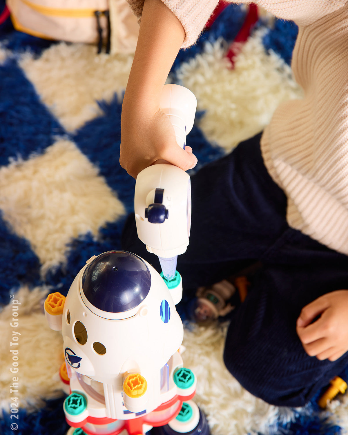 Child playing with a toy drill on a checkered floor