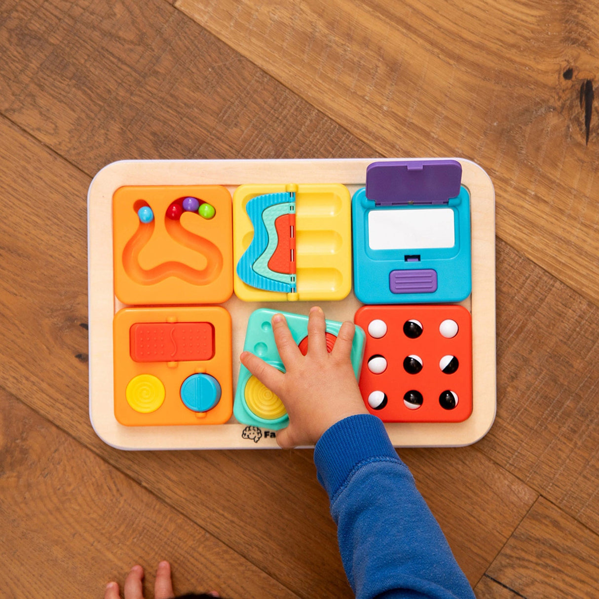 PlayTab - Modular, Sensory, Activity Board with various shapes and a child's hand interacting with it on a wooden surface.