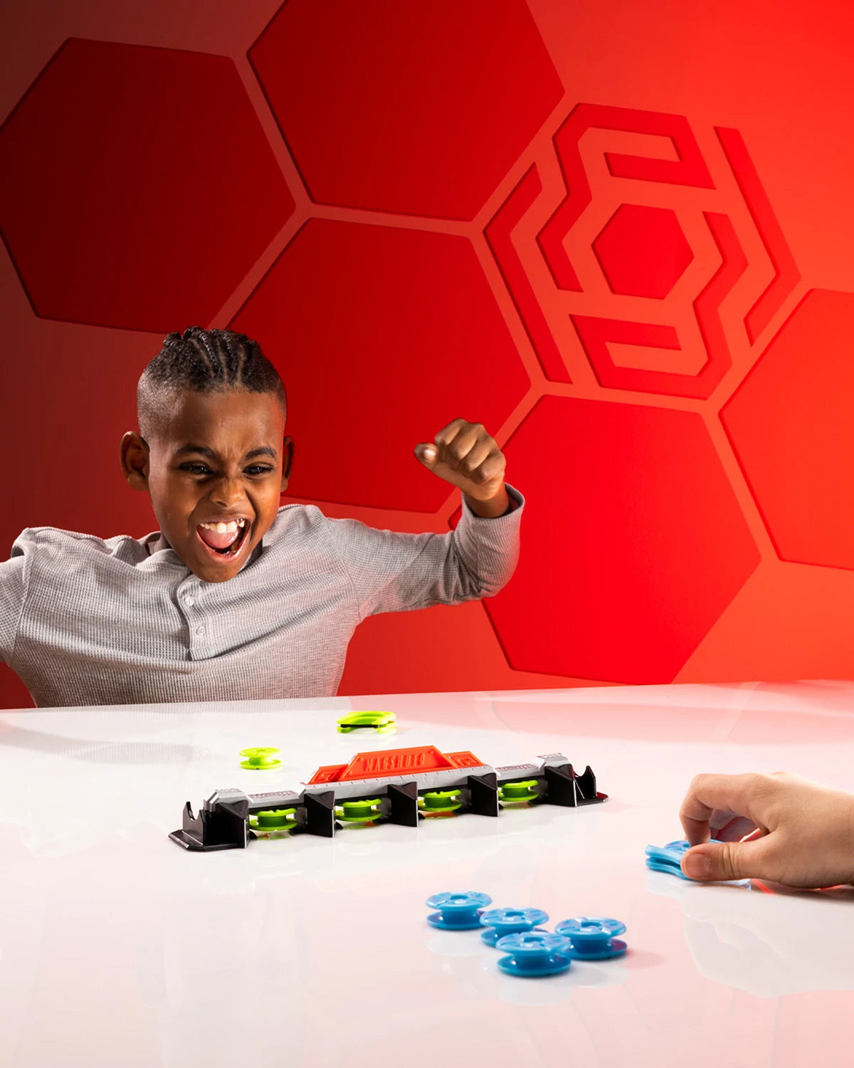 Child playing with a Magshuto Knockout Rail game against a red geometric-patterned wall.