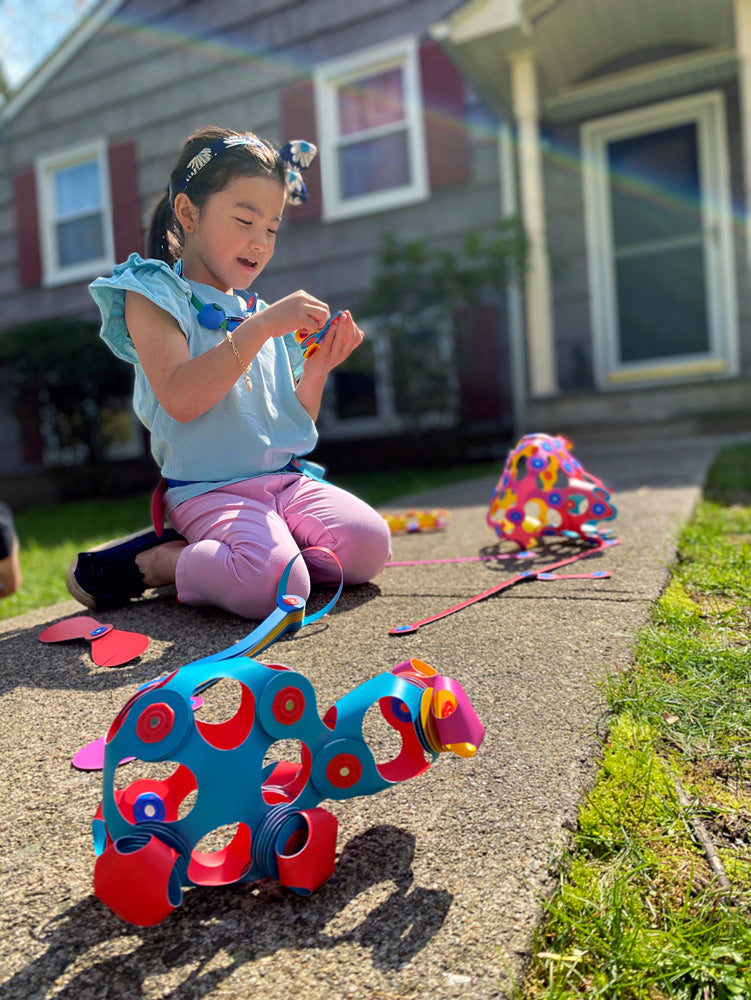 Child playing with colorful Clixo Rainbow Pack on a sidewalk with a house in the background