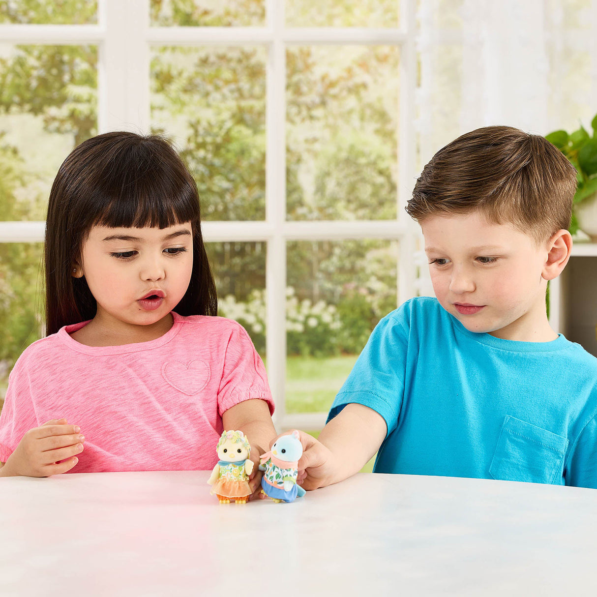 Two children playing with Calico Critters Citrus Bird Family on a table in a bright room.