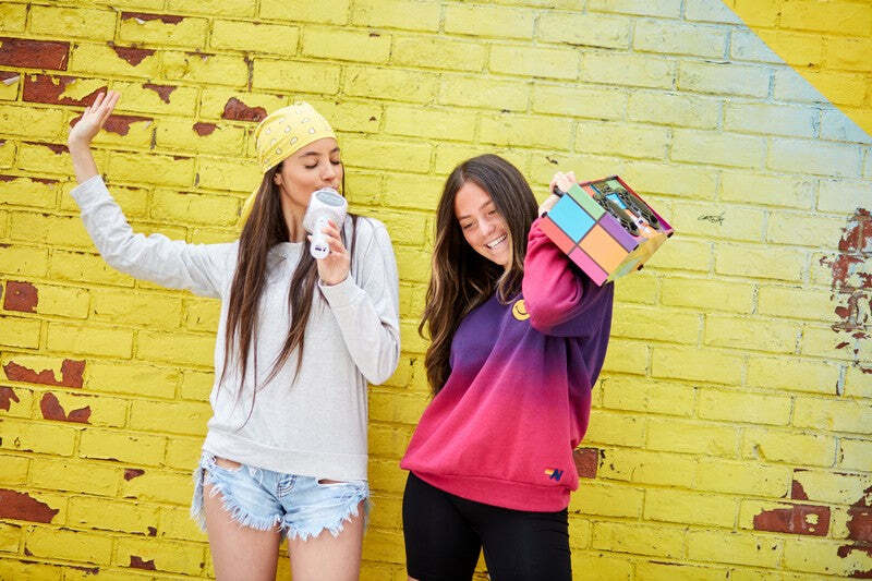 Two people posing against a yellow brick wall with colorful boom box and a Silver Bling Karaoke Microphone.