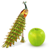 Decorative metal peacock figurine next to a green apple on a white background