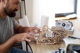 Man assembling a wooden mechanical model on a desk.