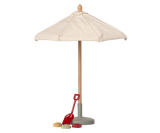 A miniature toy Maileg Sunshade, Miniature with a cream fabric canopy, a light wood pole, a gray base, and a small red shovel accessory on a plain white background.