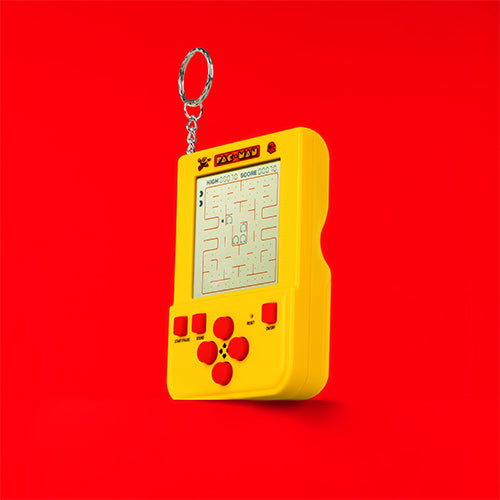 A PAC-MAN Keyring Arcade Game handheld electronic game console  in bright yellow with red buttons and a silver keyring, shown against a solid red background.