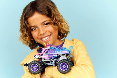 Child holding a LEGO Technic: Monster Jam™ Sparkle Smash™ Pull-Back against a light blue background