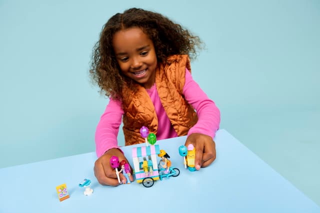 Child playing with LEGO Friends: Ice Cream & Balloon Stand set on a light blue background