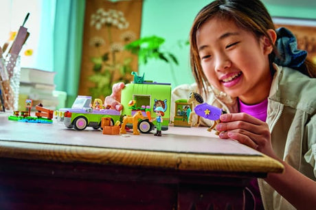Child playing with LEGO Friends: Horse & Baby Foal Trailer figures and vehicles on a desk