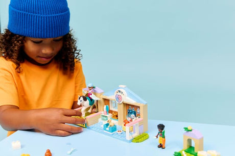 Child playing with a LEGO Friends: Animal Vet Clinic set on a light blue background