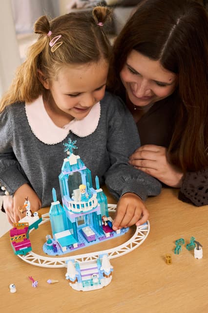 Child and adult playing with a LEGO Disney Princess: Elsa's Ice Castle & Snow Ride Adventure set on a wooden table.
