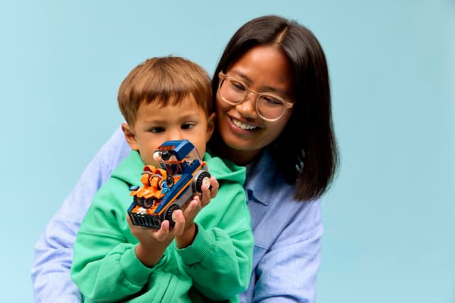 Woman and child holding a LEGO City Great Vehicles: Motorcycle Transporter against a light blue background