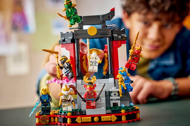 Child playing with a LEGO Ninjago: Ninja Character Display 15th Anniversary set featuring various characters and a temple-like structure.