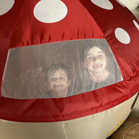 Children peeking from a Mushroom House Air Fort with a clear panel.