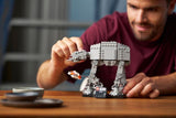 Man building a LEGO model of an AT-AT walker on a wooden table.