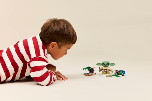 Child playing with LEGO Star Wars: Grogu's Homestead figures on a plain background
